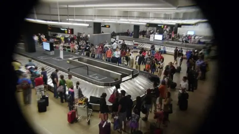 Travelers Standing Around the Luggage Carousel at the Airport Waiting for Their Luggage to Appear