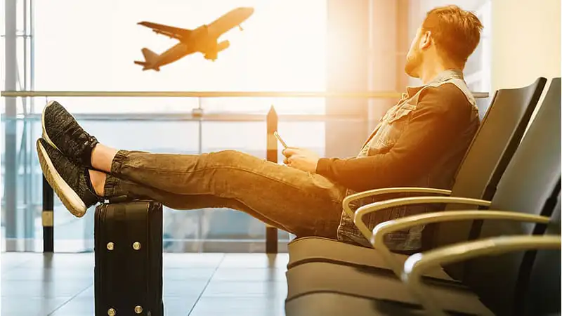 A person waiting at the airport with his black luggage