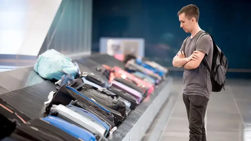 A traveler standing near a luggage conveyor and looking for his luggage